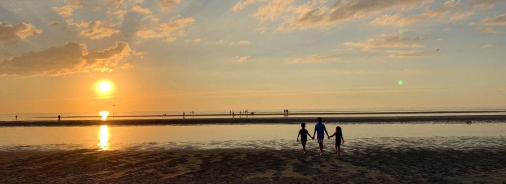A family of three walks along a beach at sunset in Cape Cod.