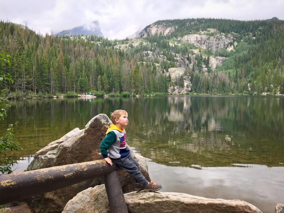 A young boy sits among large boulders while looking off into the distance while explore the Rocky Mountain National Park, a great stop on our one-week Colorado itinerary for families.
