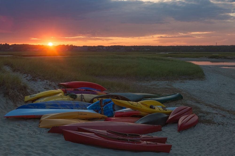 Several colorful kayaks rest on a sandy beach at sunset near Wells, Maine.