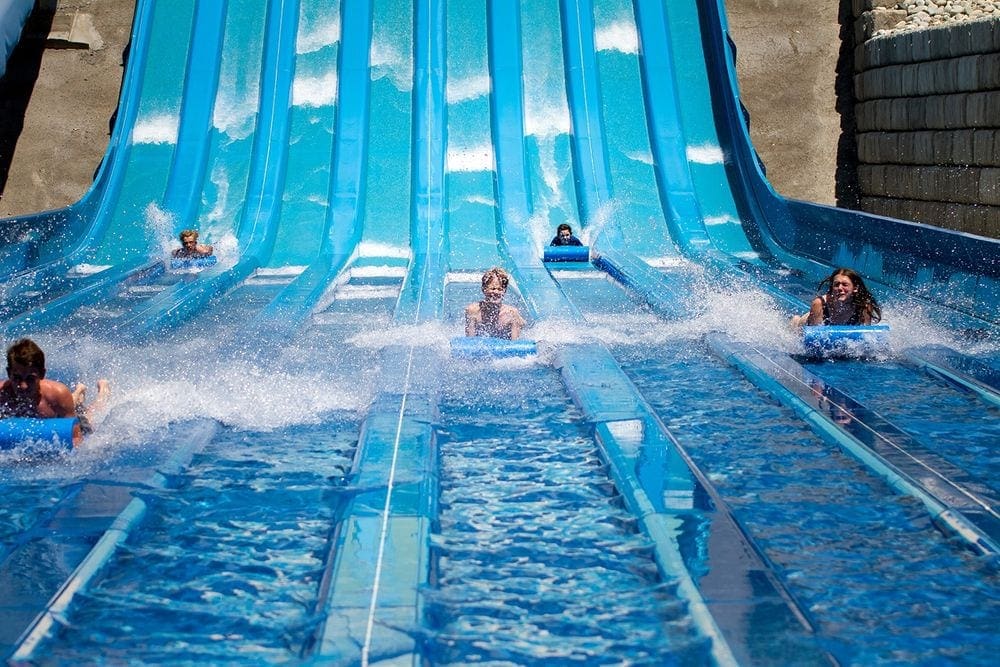 Several kids slide down a huge blue slide at Water World, one of the best things to do in Colorado with kids.