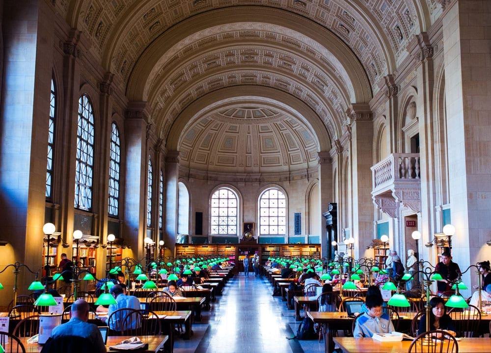 Inside a room at the Boston Public Library, featuring high ceilings and amble desk spaces.