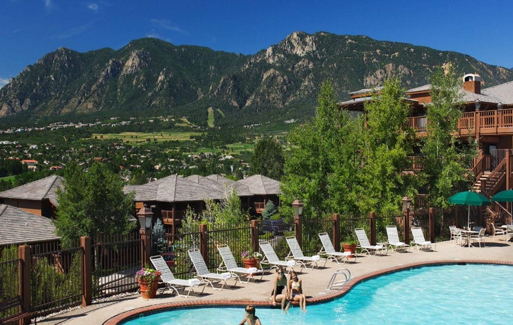 Two people sit at the side of the hotel pool with other buildings behind them at Cheyenne Mountain Resort Colorado Springs, A Dolce Resort.