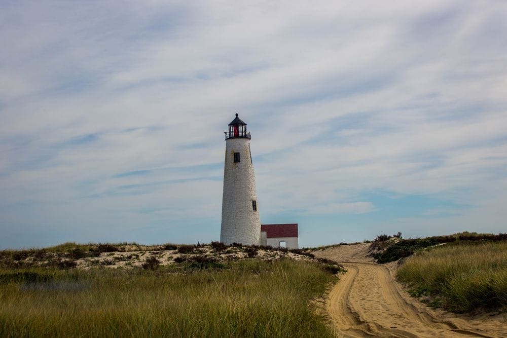 The Great Point Lighthouse stands proudly among coastal grasses and sand on an overcast day.