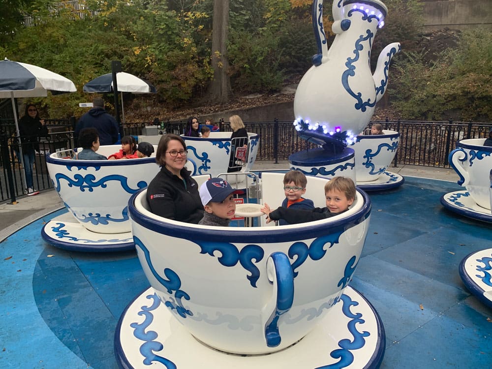 A mom and three young boys sit inside a tea-cup while enjoying the rides at Hershey Park.