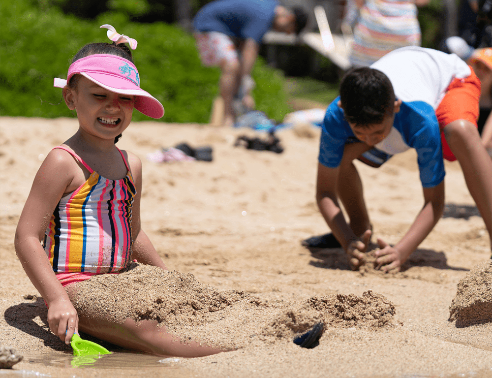 Two kids in colorful swimsuits play together in the sand on Hanauma Bay.