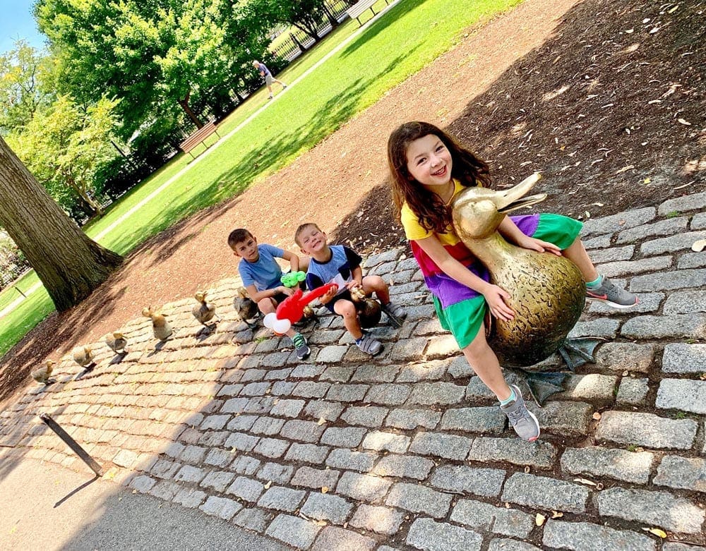 Three kids sit amongst the iconic statue of Ducks in Boston, one of the best spring break destinations for families around the world.