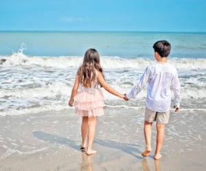 Boy and girl holding hands and walking to the beach.