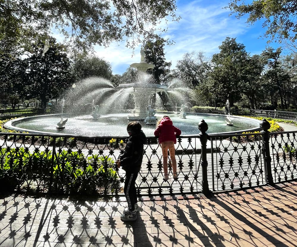 Two kids marvel at a fountain in Savannah on a sunny day.