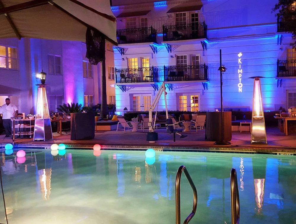 The outdoor pool at the The Kimpton Brice Hotel lit up with several colors at night.