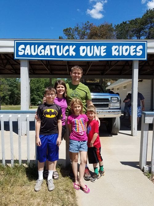 A family of five poses together in front of a sign reading "Saugatuck Dune Rides".