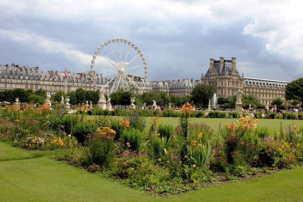 Lush gardens at the Jardin des Tuileries with a ferris wheel and other Parisian buildings in the distance.