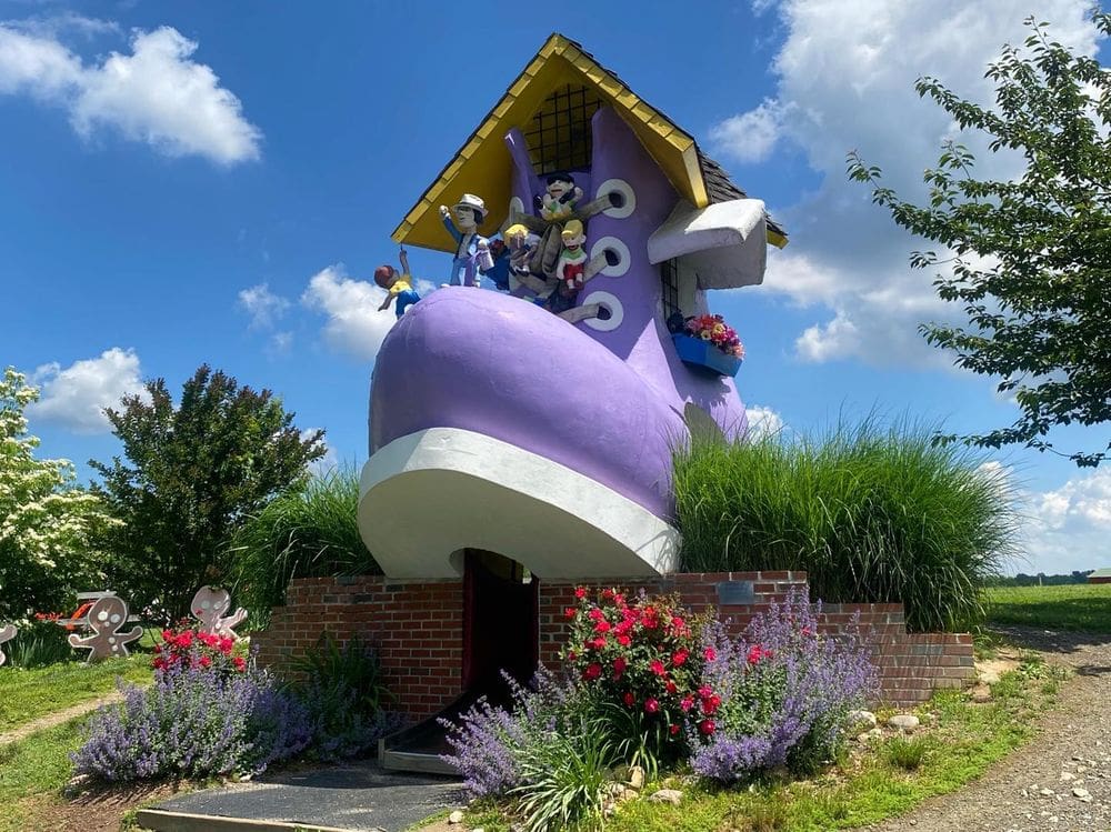 A large state of a purple shoe with several people coming out of it sits above flowers at Clark's Elioak Farm.