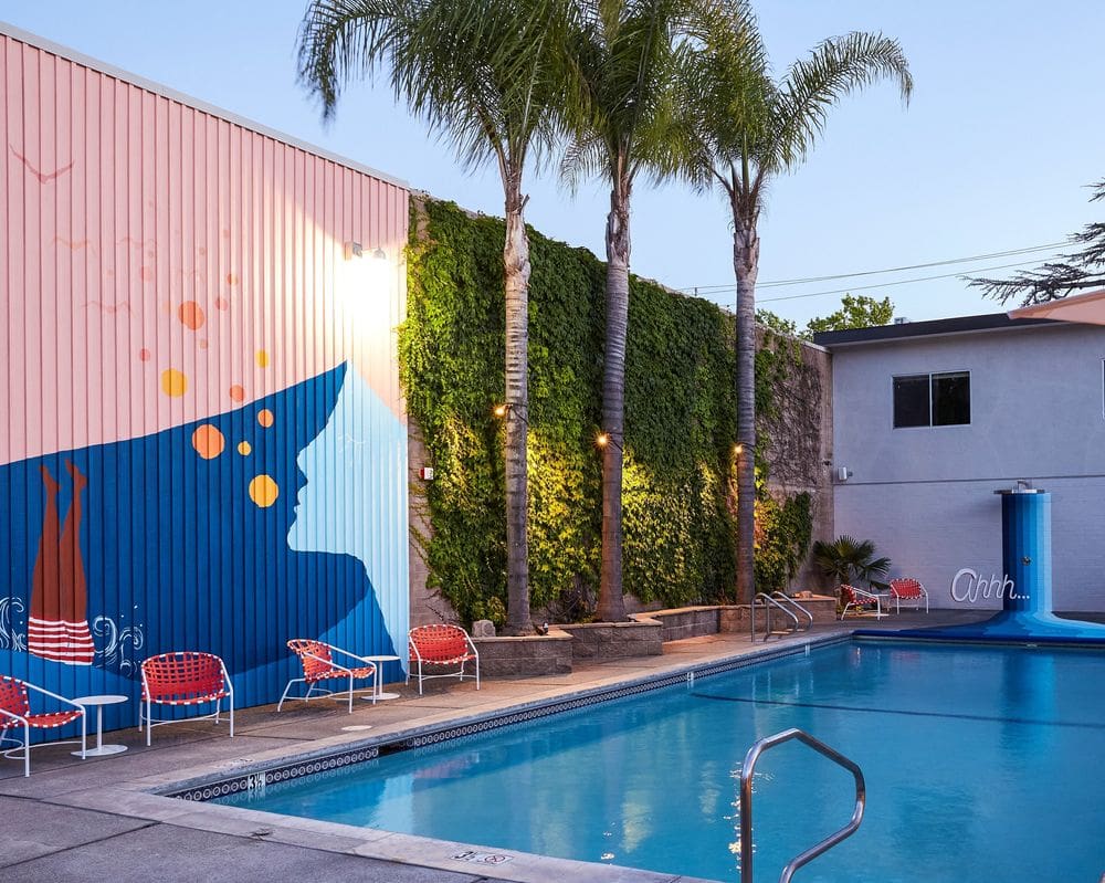 A view of a pool surrounded by colorful walls, furniture, and swaying palms.