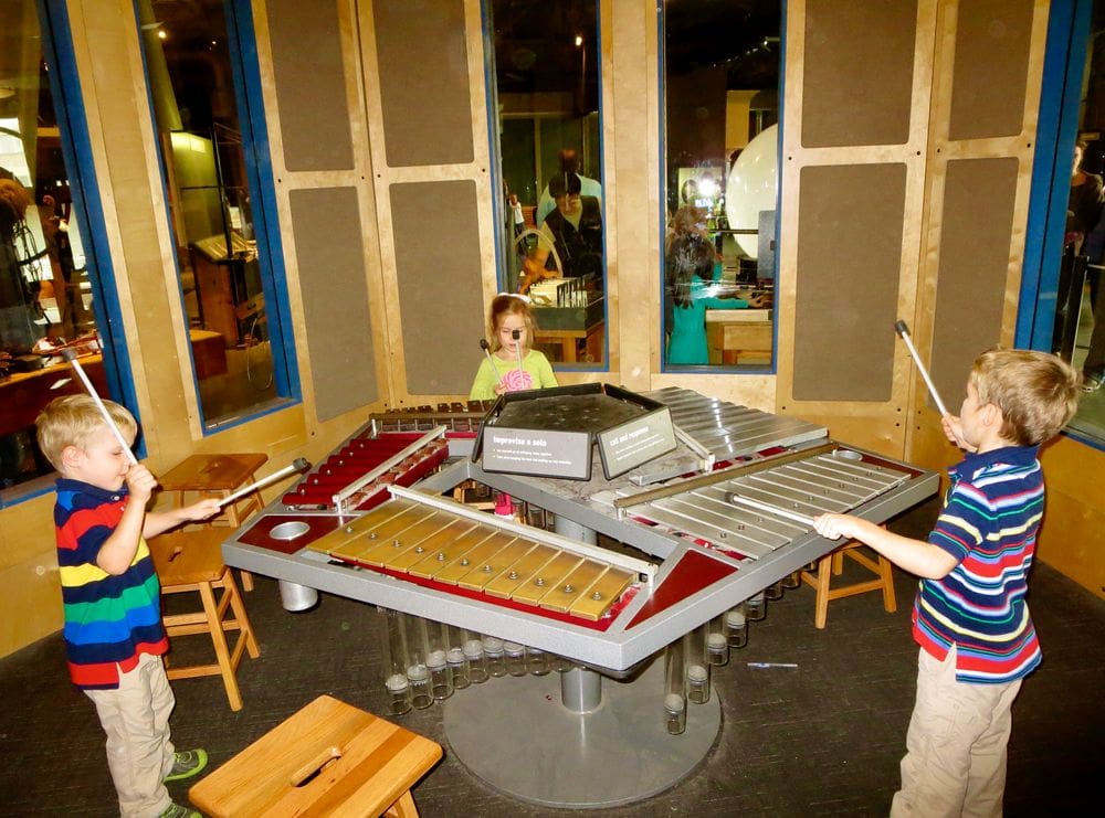 Three kids play on a large xylophone while exploring the Exploratorium.