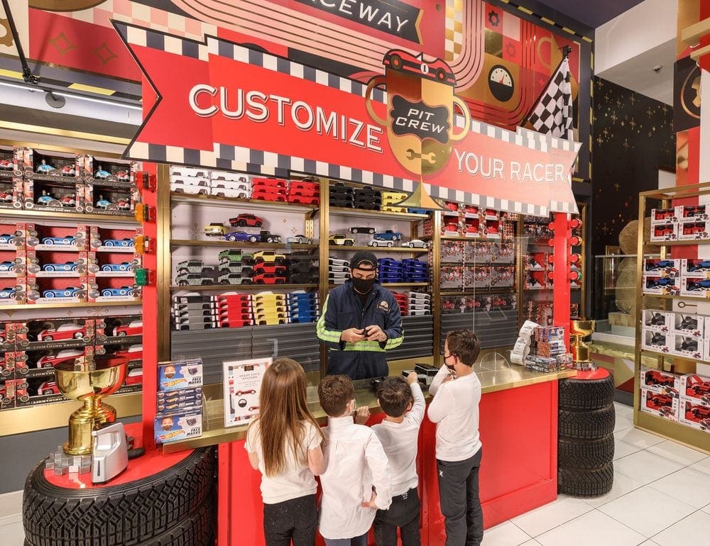 At one of the best indoor New York City activities for kids, four kids watch a staff member make a customized race car for kids at FAO Schwarz.