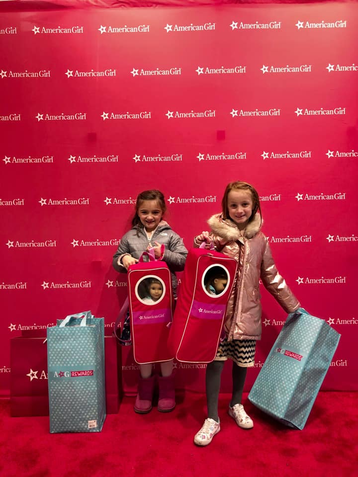 Two girls stand with their American Girl dolls while explore the store.