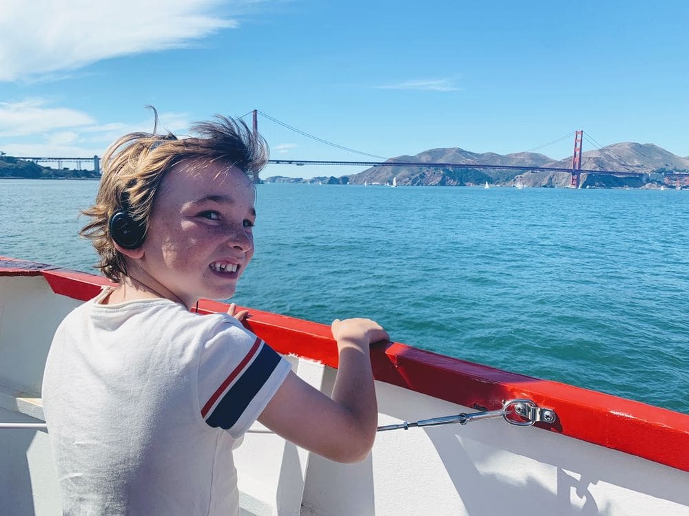 A young boy wearing headphones enjoys a view of the San Francisco Bay with the Golden Gate Bridge in the distance.