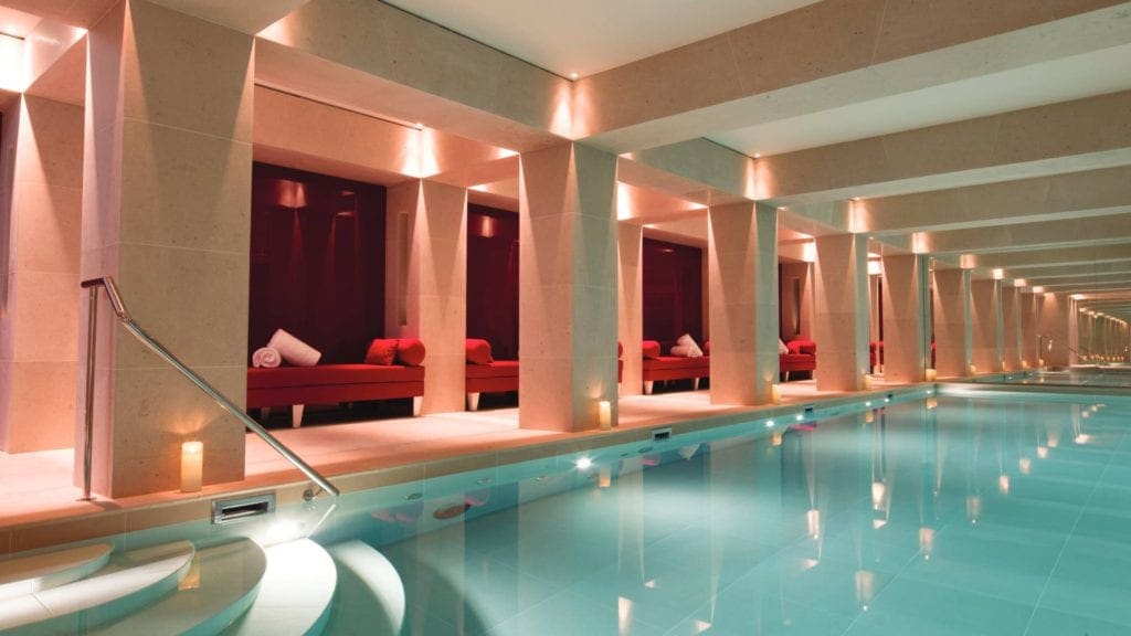 The indoor pool at the La Réserve Paris Hotel and Spa, featuring red alcoves with lush poolside loungers.