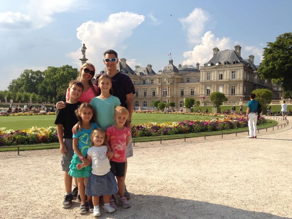 A family of six poses together with the Palace of Versailles behind them.