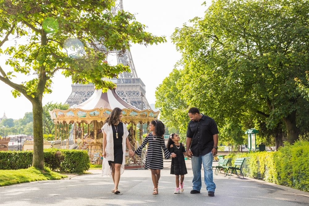 A family of four walks hand -in-hand with the iconic Paris carousel and Eiffel Tower in the distance.