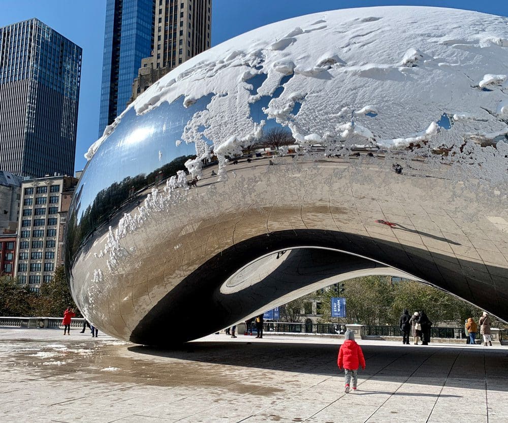 A young boy in a red coat stands in front of the iconic Bean in Chicago.