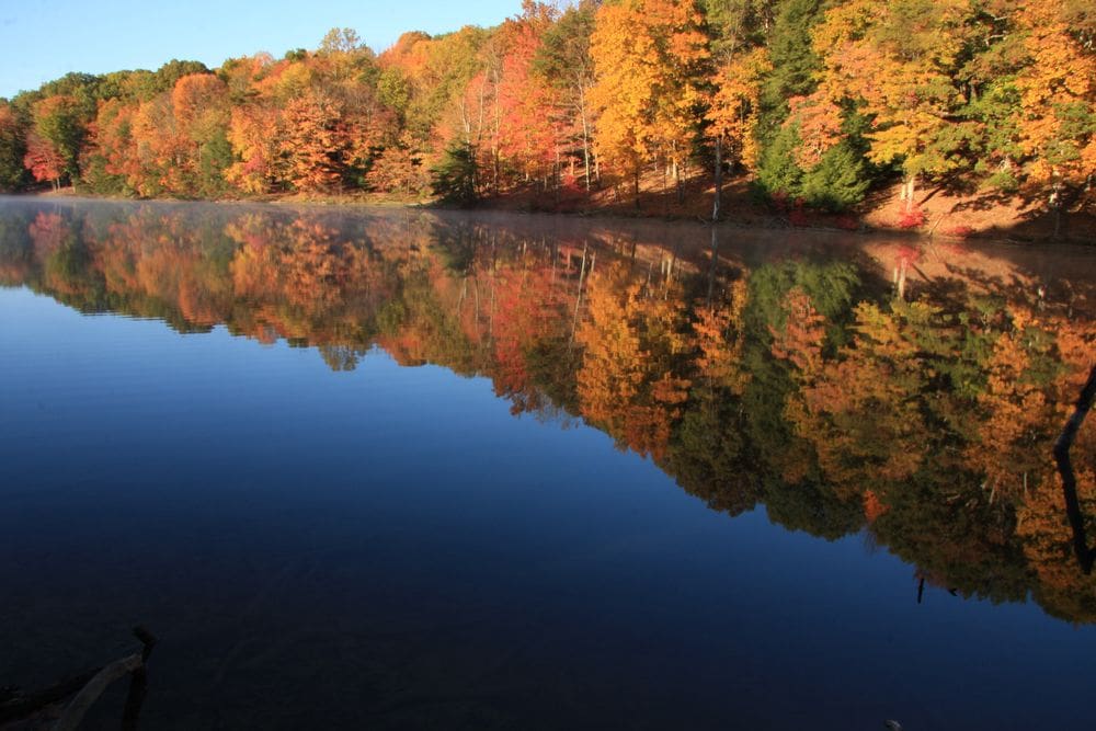 A water reflects the vibrant fall colors of the trees on Rose Lake near Hocking Hills State Park.