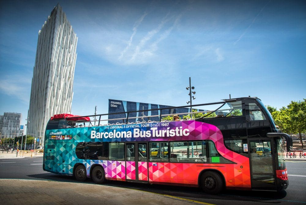 One of the brightly colored tour buses by Hop On Hop Off Barcelona parked in a large square, one of the best things to do in Barcelona with kids.