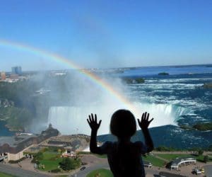 A baby looks out a window onto a rainbow over Niagara Falls.