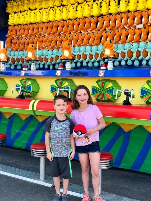 Two kids stand together in front of a colorful carnival game at Coney Park, one of the best New York City outdoor activities for kids.
