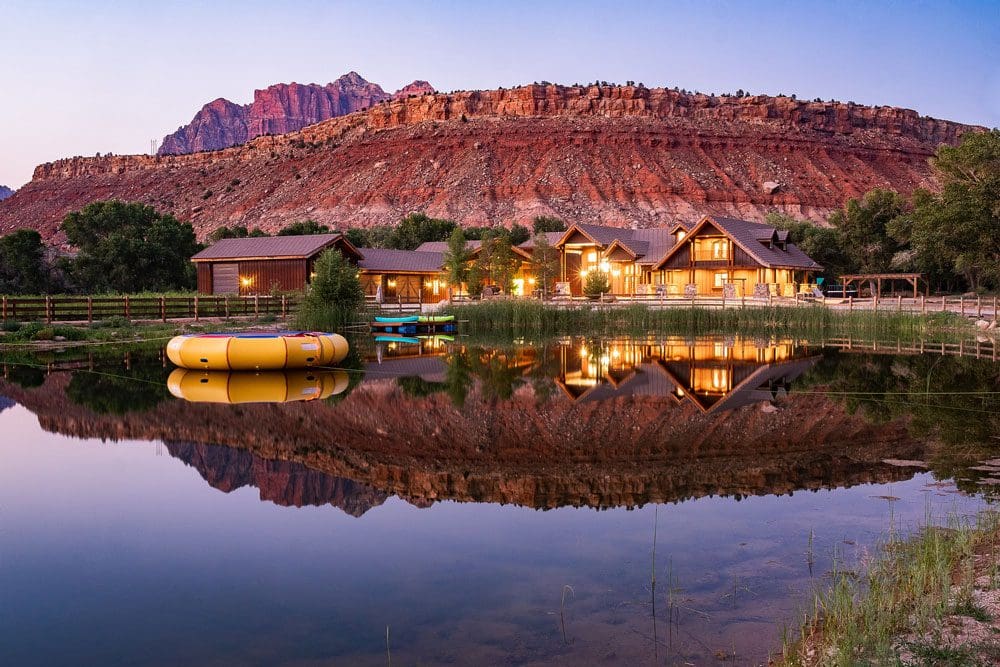 Across a lake, reflecting the desert scene, are the hotel buildings for Red Rock Inn Bed and Breakfast.