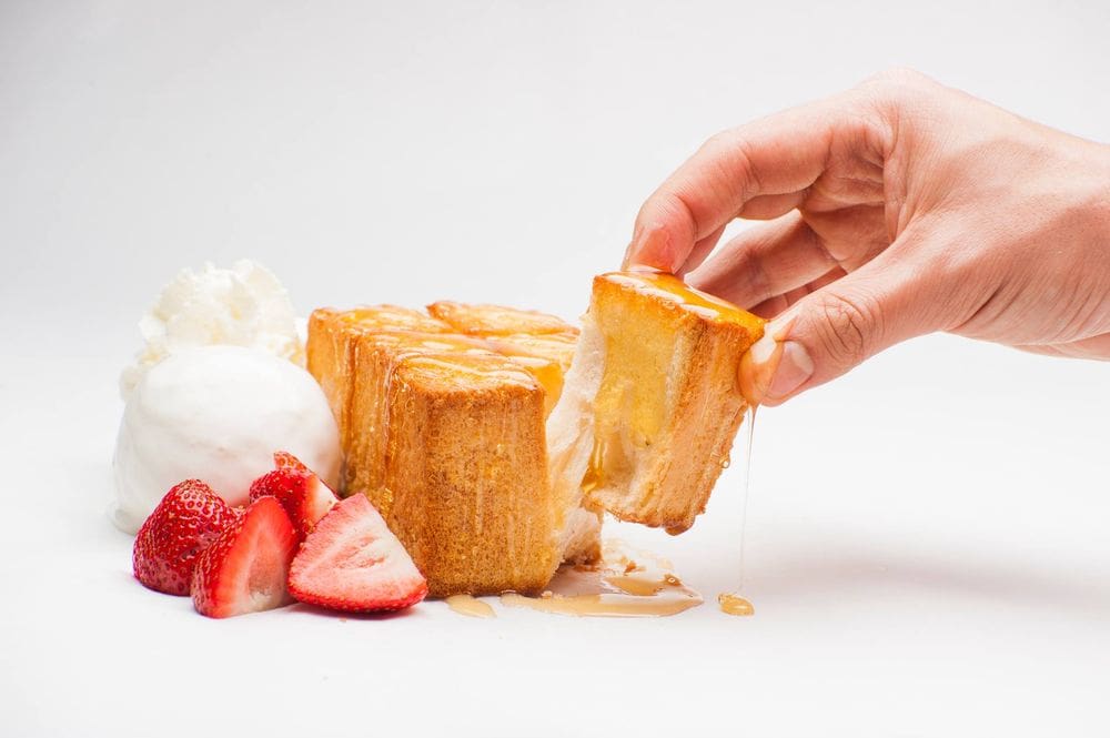 A white hand reaches out to pull off a cub of sticky bun, while ice cream and fresh strawberries rest on the other side at Spot Dessert Bar.
