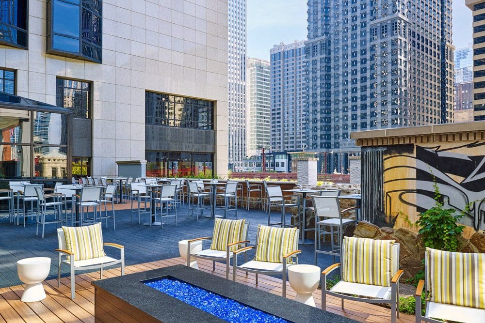 A rooftop terrace at the The Westin Chicago River North, featuring a fire pit, several seating areas, and a great view of the surrounding buildings.