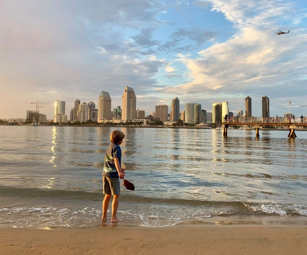 A young boy looks at the water from a beach near San Diego, with the full skyline across the bay.