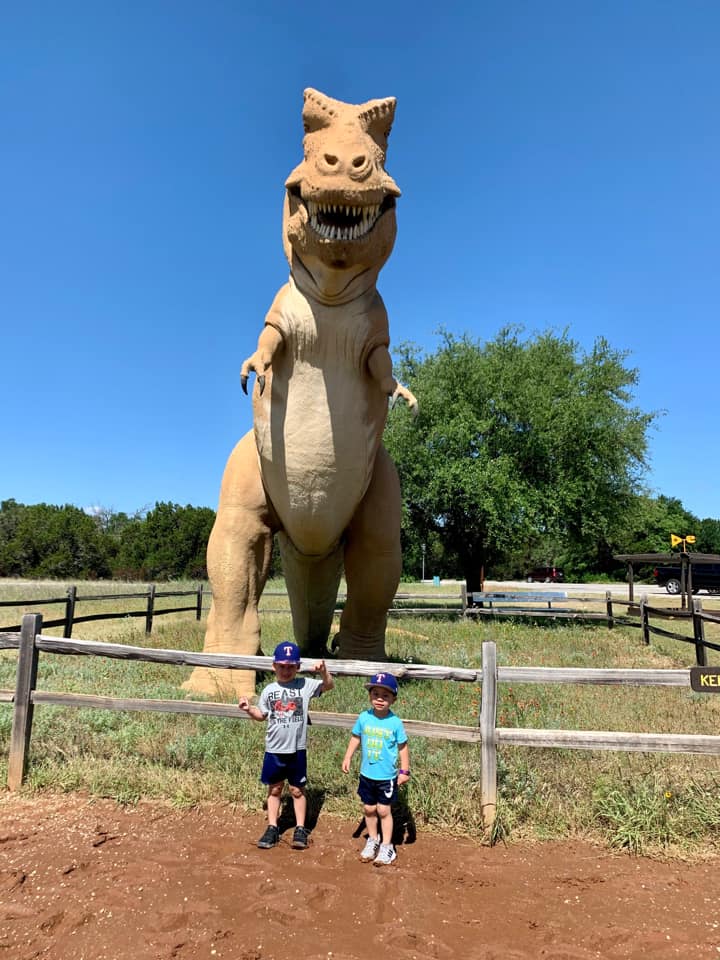 Two kids stand in front of a large T-Rex dinosaur while visiting the Dinosaur Valley State Park.