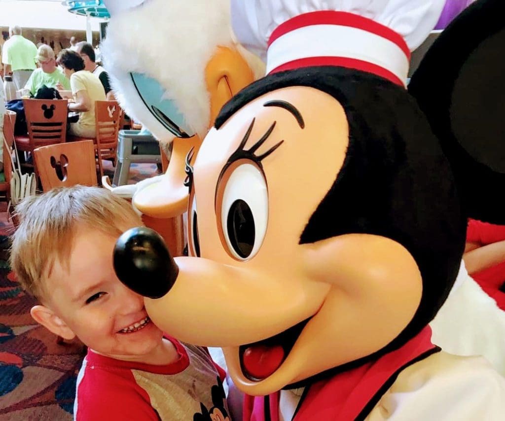 A young boy laughs as he hugs Chef Mickey Mouse at a breakfast.