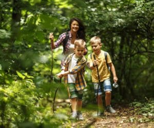 A mom and two boys hike along a shaded path amongst lush greenery.
