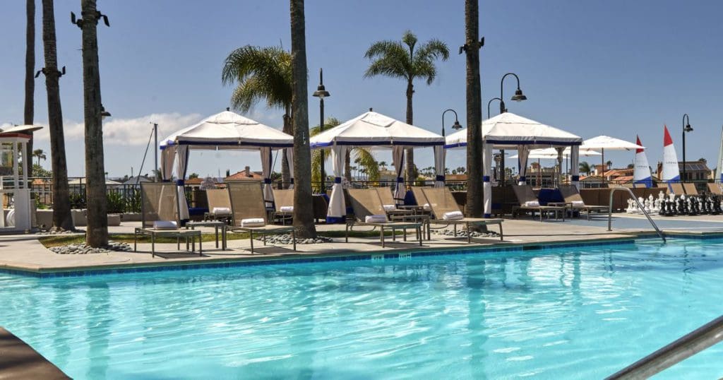 The pool and surrounding pool deck with white cabanas at the Loews Coronado Bay Resort, one of the best San Diego beachfront hotels for families.