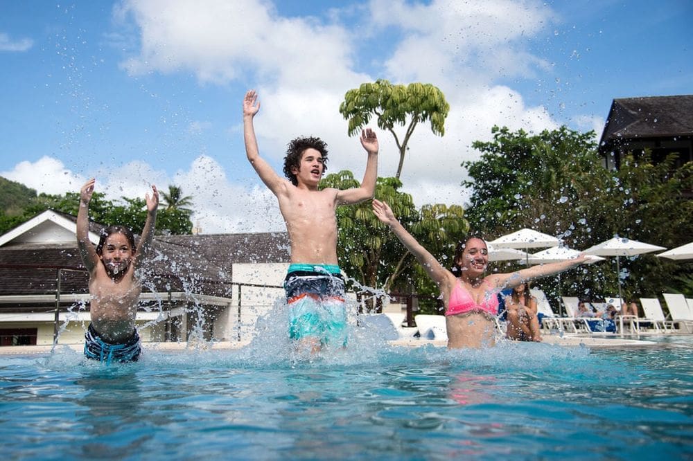 Three kids jump into the pool at the Marigot Bay Resort and Marina, creating a large splash.