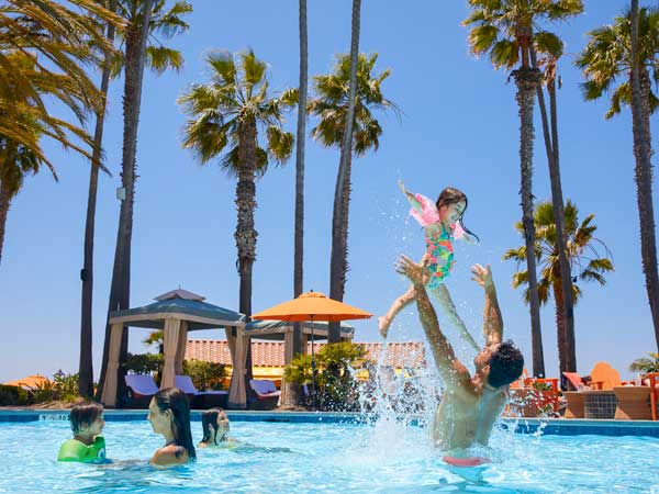 A dad throws his daughter in the air while enjoying the pool at the San Diego Mission Bay Resort, other family members swim nearby.