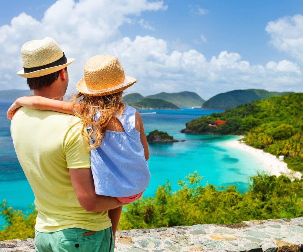 A dad and his daughter, both wearing Panama hats, look over a scenic view of the US Virgin Islands.
