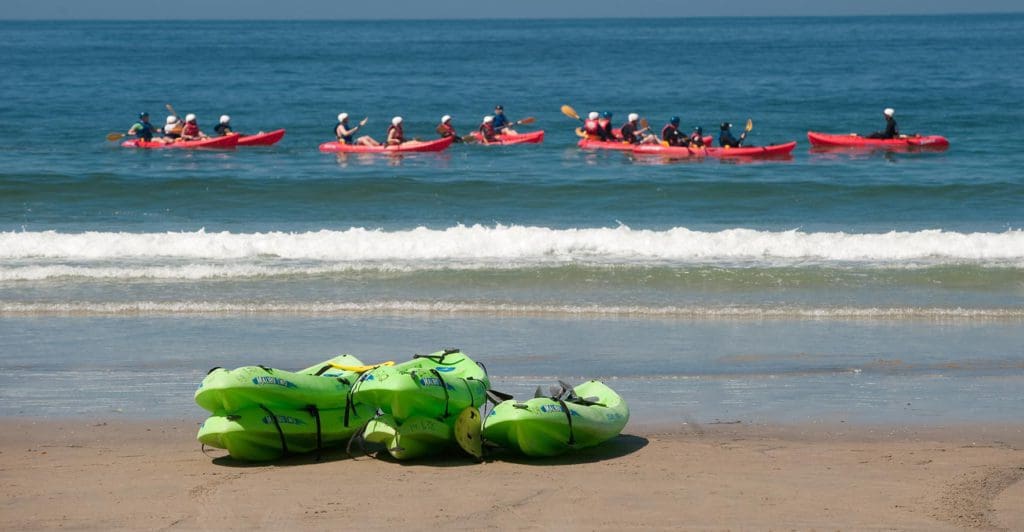 Several people kayak off-shore from La Jolla Shores Hotel, while two empty kayaks rest on shore.