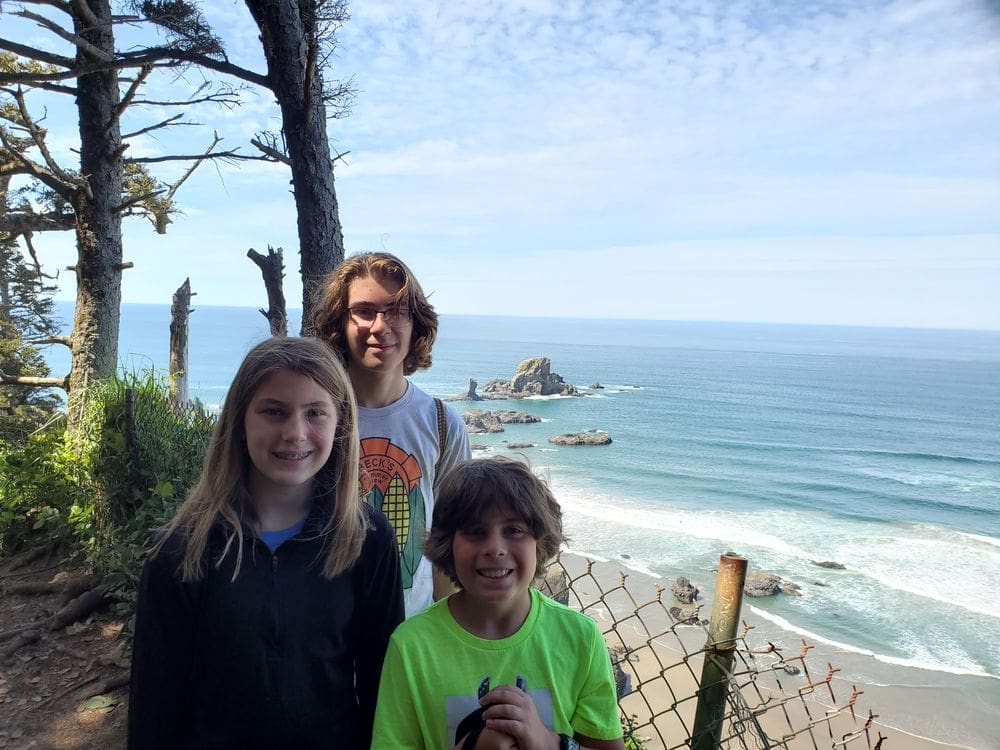 Three kids pose together with a view of Indian Beach behind them.