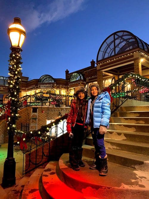 Two kids in winter gear stand on holiday-lit steps while exploring Breckenridge.
