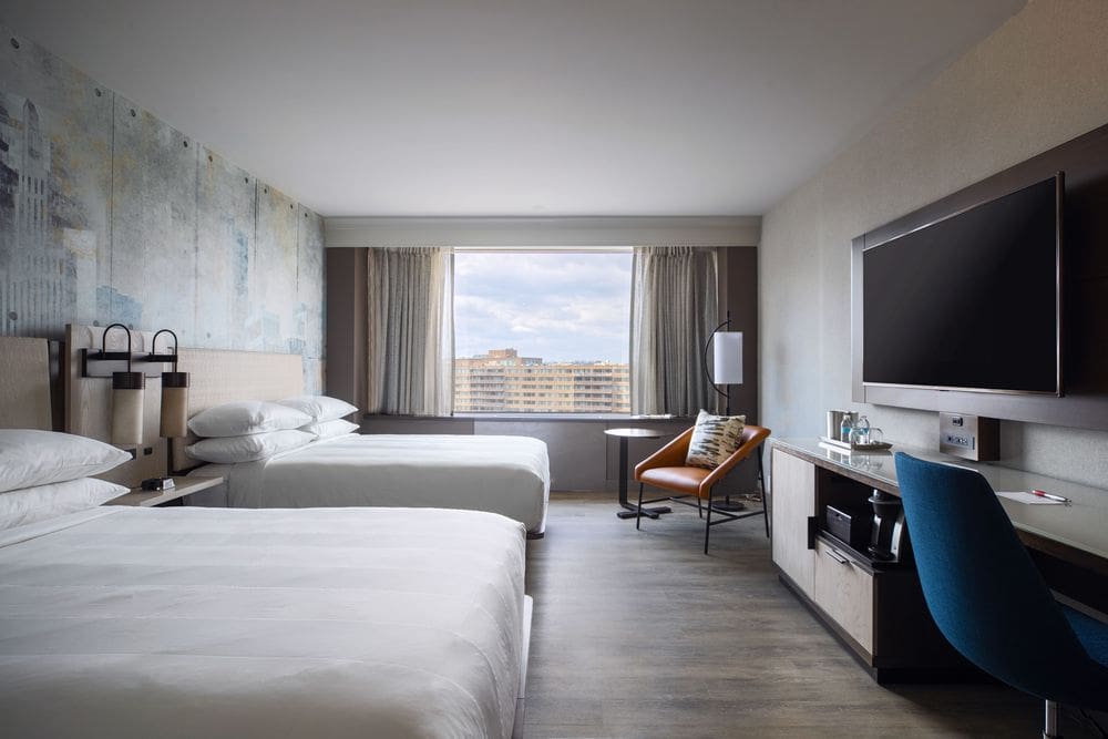 Inside one of the guest rooms at the Crystal City Marriott At Reagan National Airport, featuring two beds and natural-hued furnishings.