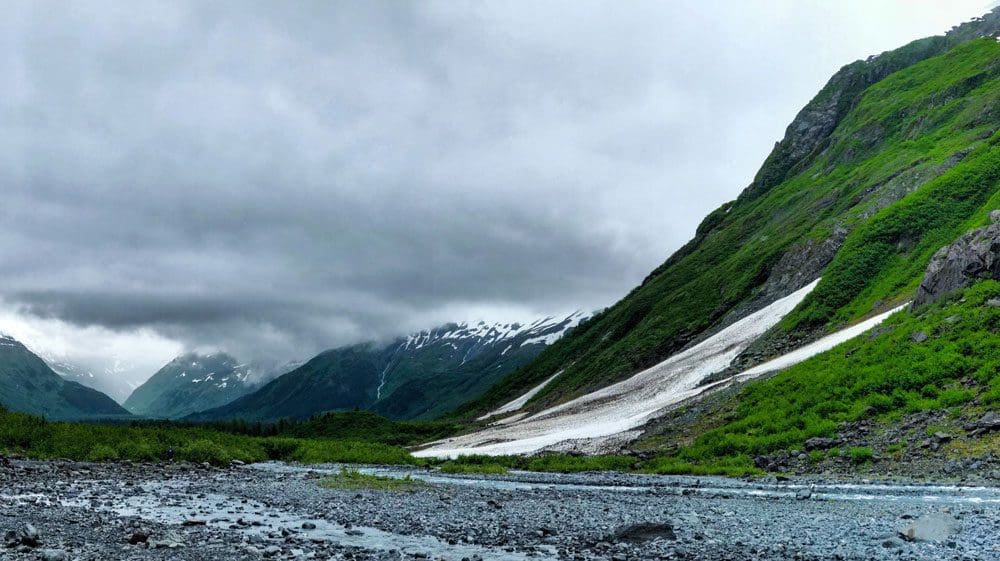 A view of a sparse glacier, surrounded by bright green foliage, at Bryon Glacier Trail near Anchorage.