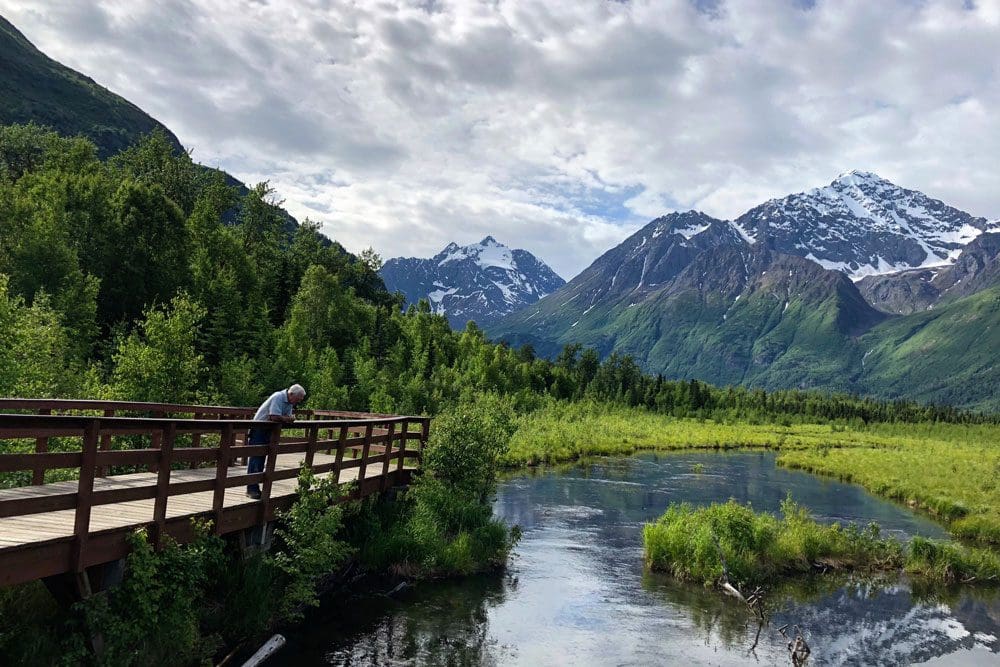 A man leans over a bridge looking into a river at Eagle River Nature Center, one of the best hikes near Anchorage for families.