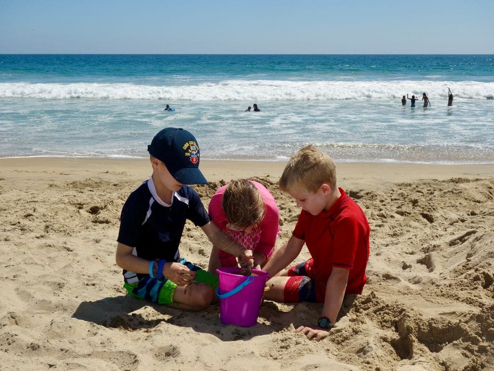 Three kids play in the sand while exploring San Diego.