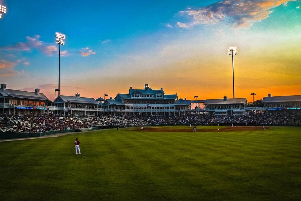 The Frisco RoughRiders ballpark at sunset, featuring several players on the field and full stands.