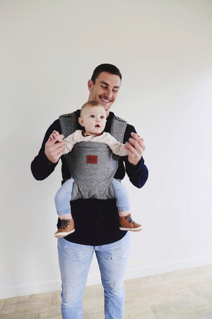 A dad plays with his child while holding her in a front carrier by Happy Baby Carrier.