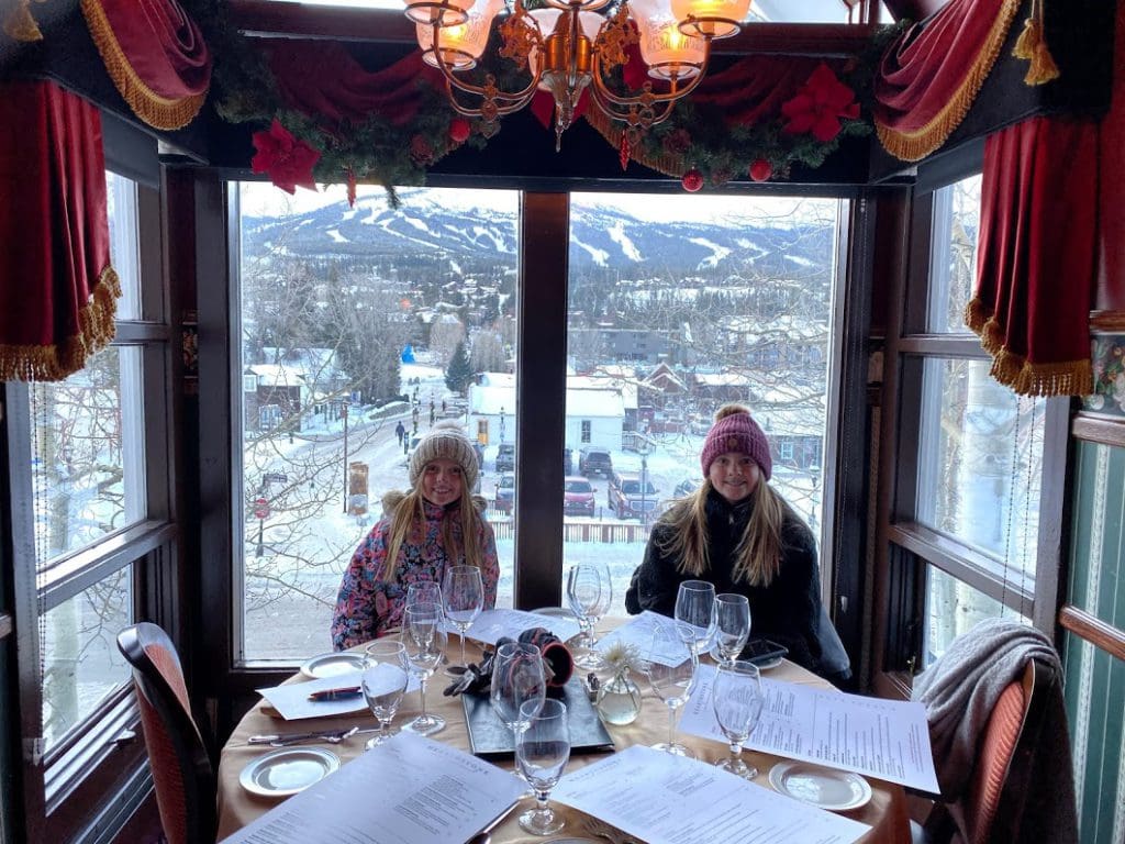 Two girls sit at a table enjoying a meal in a restaurant while enjoying a family trip to Breckenridge during the winter with kids.